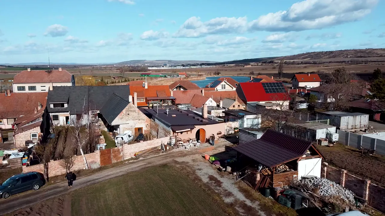 Letecký pohled na zadní část pozemku s lososovou budovou uzenářství, za vesnicí rybník a kopce