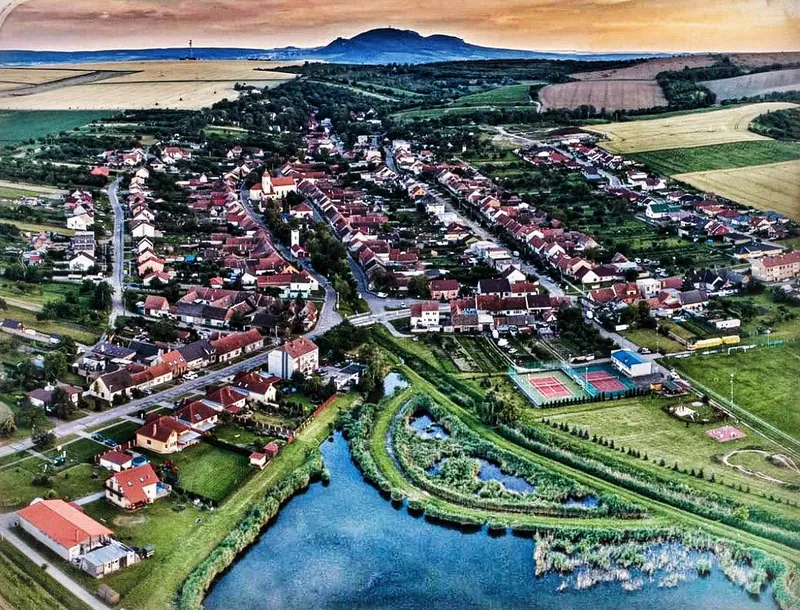 Starovice z výšky: obec s kostelem, rybník a pole kolem